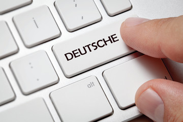 White computer keyboard and blue button against Deutsche background.Male hand pressing Deutsche written button on computer keyboard.