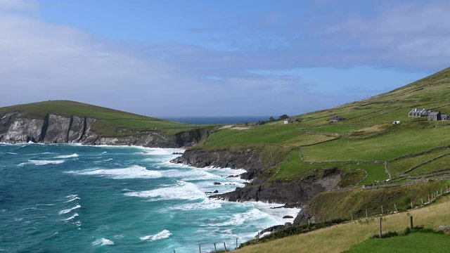 Turquoise color water and white waves of North Atlantic Ocean at Irish coast, Dunquin village on the green hill slope.