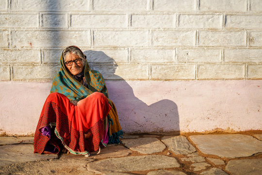 Old aged woman sitting with the support of the wall in the sunset wearing glasses