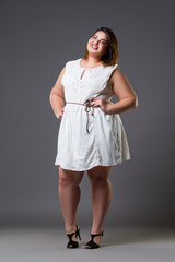 Happy plus size fashion model in casual clothes, fat woman on gray background