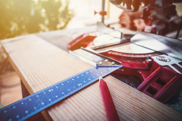 A wooden table full of woodworking tools. Red pencil, meter, angle and miter saw. Craft work theme.