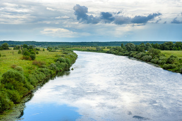 a river flowing between green banks under clouds