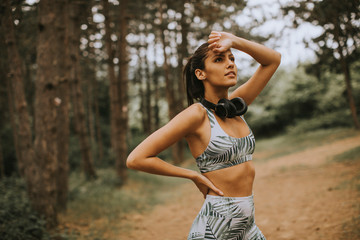 Young beautiful female runner listening to music and taking a break after jogging in a forest