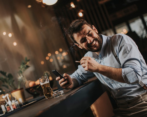 Man drinking beer, smoking cigarette and looking at mobile phone at the pub