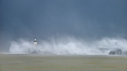 Massive waves crash over harbour wall onto lighthouse during huge storm on English coastline in...