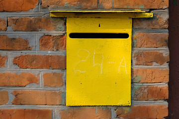 Old Metal yellow personal mailbox in a red brick wall. Box for receiving letters and other paper mail. Hole in the drawer for receiving correspondence near the house.