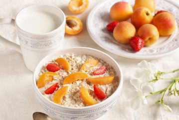 breakfast with oatmeal and fruit, apricot and strawberries with milk. Summer season, fresh fruits, copy space