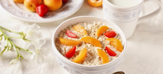 breakfast with oatmeal and fruit, apricot and strawberries with milk. Summer season, fresh fruits, copy space