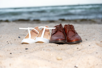 Two pairs of ladies and gentlemen shoes on the beach in front of water