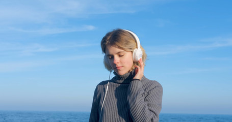 Young handsome female listen to music with headphones outdoor on the beach against sunny blue sky	