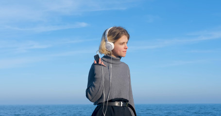 Young handsome female listen to music with headphones outdoor on the beach against sunny blue sky	