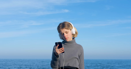 Fototapeta na wymiar Young handsome female listen to music with headphones outdoor on the beach against sunny blue sky 