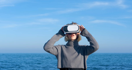 Young handsome female with virtual reality glasses outdoor on the beach against sunny blue sky	