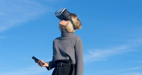 Young handsome female with virtual reality glasses outdoor on the beach against sunny blue sky	