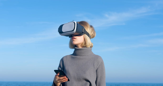 Young handsome female with virtual reality glasses outdoor on the beach against sunny blue sky	 - Powered by Adobe