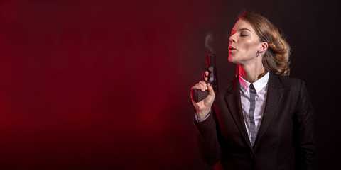 blowing smoke out of a gun after a shot. portret of a business woman on a dark background. banner...