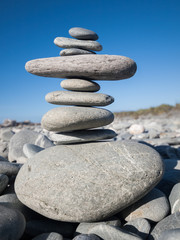 Fototapeta na wymiar A beautiful rock and beach stone pebble stack on a pebble beach with a vivid blue sky background. Zen, mindfulness, meditation and relaxation. Stones have unique healing properties.