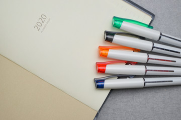 Set of colorful pen placed on 2020 planner book on gray cement texture background. Task management concept.