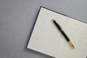 Black and gold fountain pen placed on calendar notebook on gray cement texture background. Task management concept.