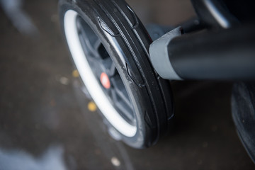 A baby pram stroller pushchair wheel tyre,  in a wet rainy dirty city sidewalk pavement...