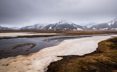 Meadow with snow and frozen lake and snowcapped mountains. Iceland