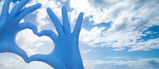 Medicine concept with heart build hands in medical gloves on blue sky background