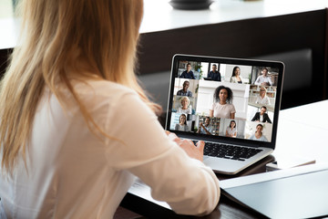Back view of businesswoman sit at desk have video call with multiracial colleagues on laptop,...