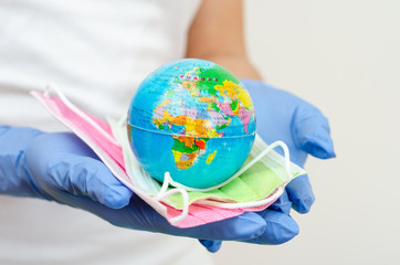 Hands covered with surgical gloves holding earth  globe and face masks representing the concept of protecting  population against disease transmission and coronavirus.