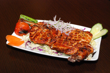 grilled half a chicken on the plate with onion and vegetables