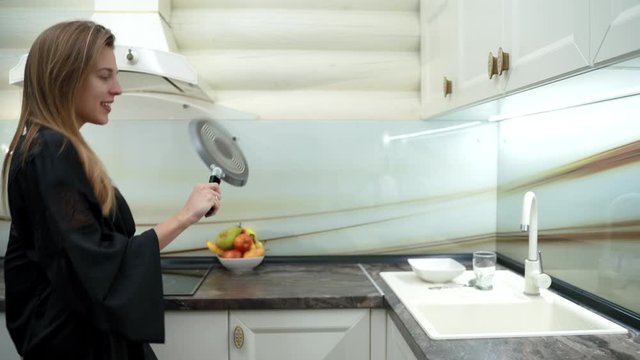 Beautiful woman dance in kitchen with a pan