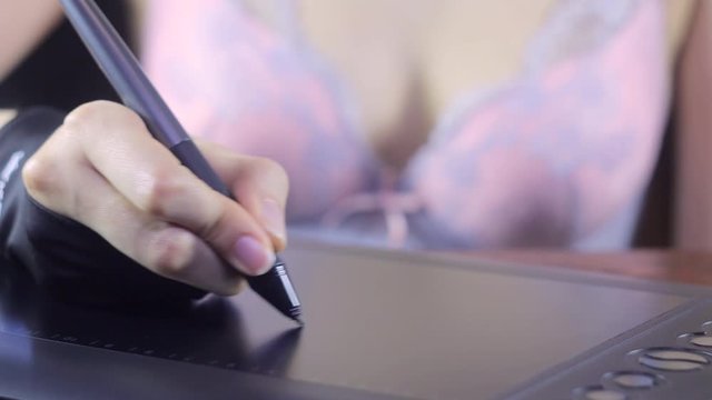 A woman in her underwear draws on a graphics tablet. Sexy girl in a bra works at home. Freelance, remote, designer, artist, affectionate, breast, sensual, intimate, workplace, bedroom, slim, create.