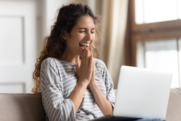 Fototapeta na wymiar Excited woman looking at laptop screen, rejoicing good news, happy laughing girl reading email or message in social network, win online lottery, great shopping offer, sitting on cozy sofa at home