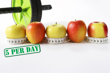 Healthy life concept. Multicolored apples with measure tap and ab wheel on white background