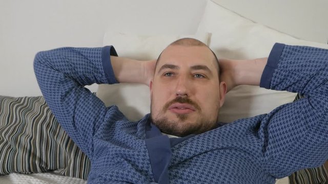Portrait of a obese man with difficulty doing exercises on the bed. Lazy man and sport
