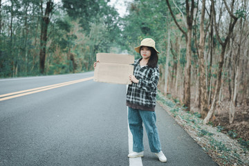 Travel hitchhiker woman holding sign with hat and backpack standing on a road