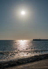 Fototapeta premium Clear sky and bright sunset over the sea with a breakwater and a lighthouse
