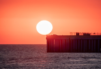 Beautiful red and orange sunset over the sea. The sun goes down over the sea. Silhouette of a pier with fishermen at sunset