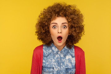 Wow, unbelievable! Closeup portrait of excited amazed woman with fluffy curly hair looking with mouth open in surprise, shocked facial expression. indoor studio shot isolated on yellow background