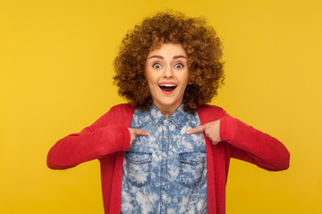 Wow, this is me! Portrait of amazed happy woman with curly hair pointing herself, looking surprised and boasting own success, proud of achievement. indoor studio shot isolated on yellow background