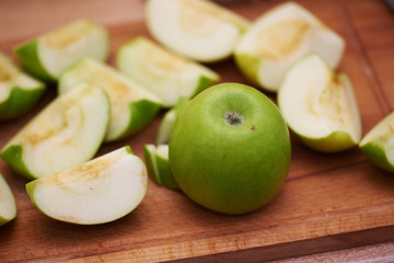 Green apples sliced far away lie on a wooden tabletop.