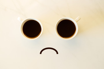 Two cups of coffees arranged as human face with line showing emotion. Sad