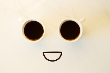 Two cups of coffees arranged as human face with line showing emotion. Smile