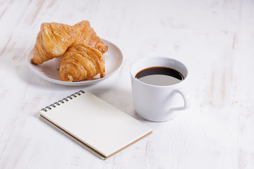 cup of hot coffee with croissant on white wooden background.  Working at home concept.