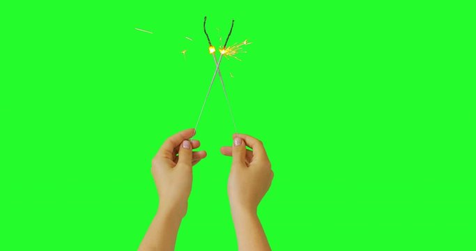 Woman or girl hands with neutral manicure holding two fireworks sparklers crossed into X sign. Keyed green screen chroma key background. Celebration holiday or new year concept. - Powered by Adobe