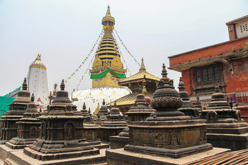 View of buddhist Swayambhunath stupa, also known among tourists as Monkey Temple, with traditional "Eyes of Buddha" painting in background and little stone stupas in foreground. Selective focus.