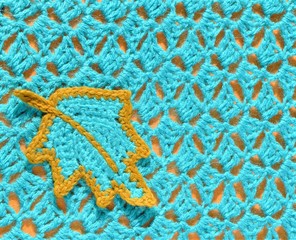 Crocheted teal leaf and crocheted pattern sample on orange background.