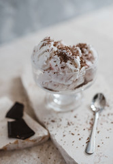 Vanilla ice cream sprinkled with chocolate chips and strawberry syrup in a transparent bowl on a light stone background