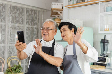 Portrait of an elderly Asian couple doing facetime video calling with a smartphone at home using...