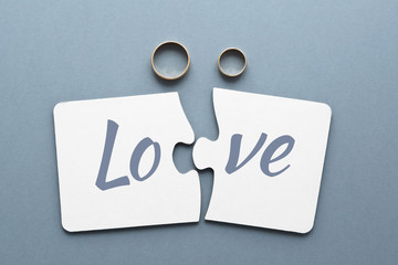 two white puzzles with the separated word love, two wedding rings on a gray-blue background 