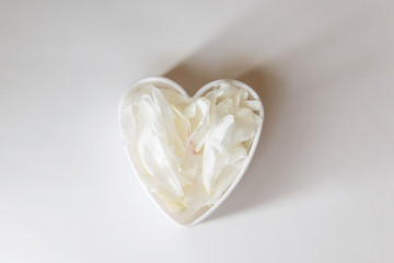 Heart shaped White peony petals decor. Peony flowers petals flat lay on a white background. Beautiful minimalistic white flowers close-up photo.